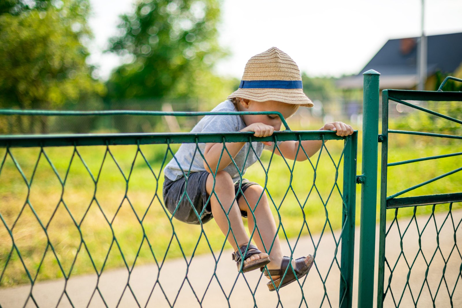 Boy in a straw hat climbing a green chain link fence gate