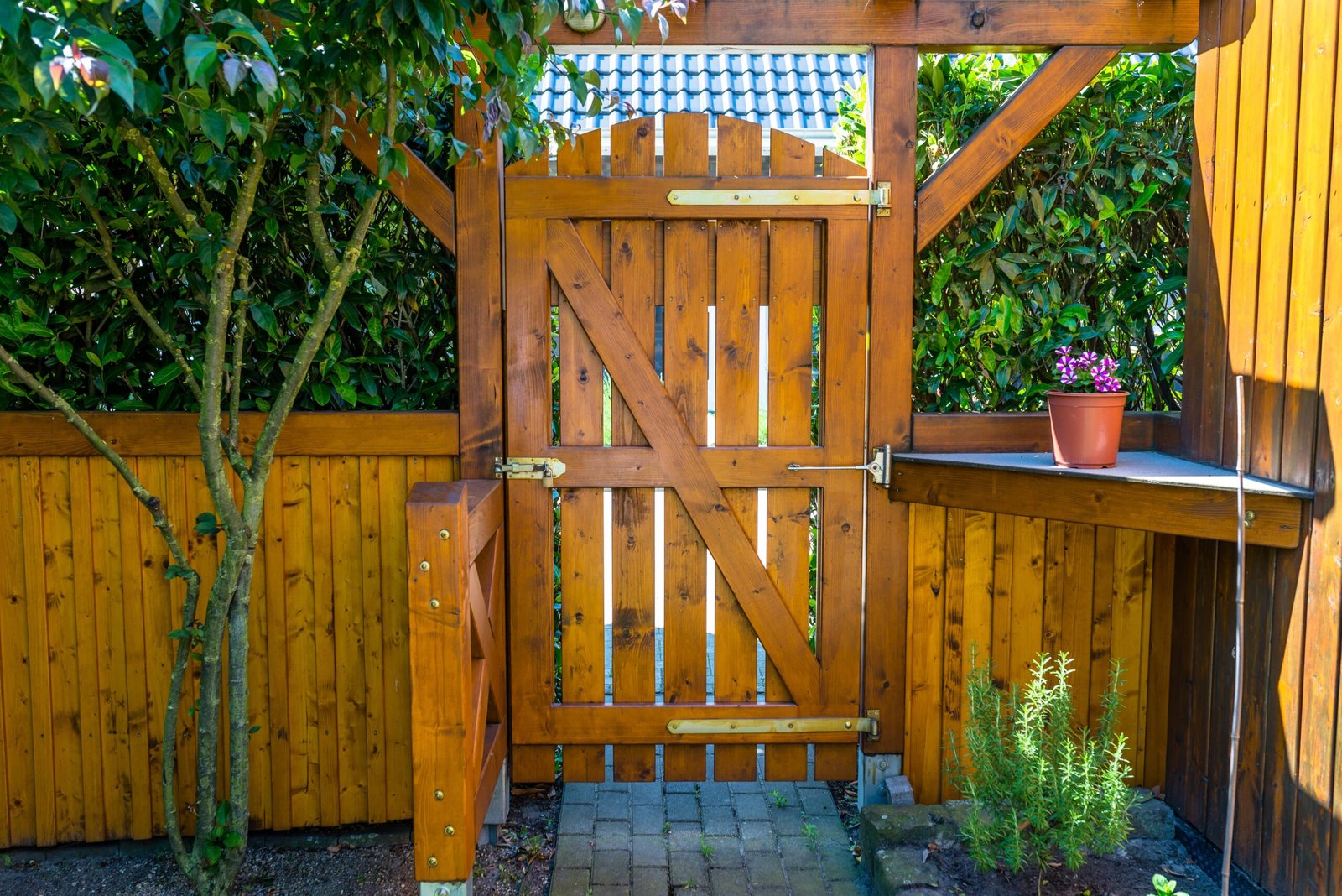 Wooden gate with brass hardware beside potted plants and hedges
